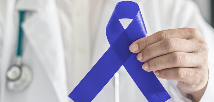 Dark blue ribbon for colon - colorectal cancer awareness on medical doctor's hand