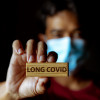 Masked Asian man show wooden sign with wording "Long Covid"