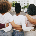 Rearview shot of a group of unrecognizable young friends walking with their arms around each other in the city