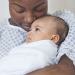 Beautiful African American mother in a hospital gown holds her newborn baby