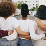 Rearview shot of a group of unrecognizable young friends walking with their arms around each other in the city
