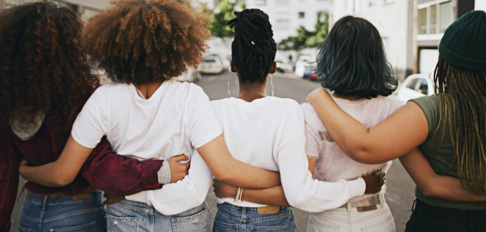 Rearview shot of a group of unrecognizable young friends walking with their arms around each other in the city