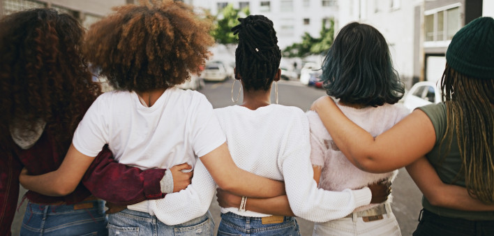Rearview shot of a group of unrecognizable young friends walking with their arms around each other in the city